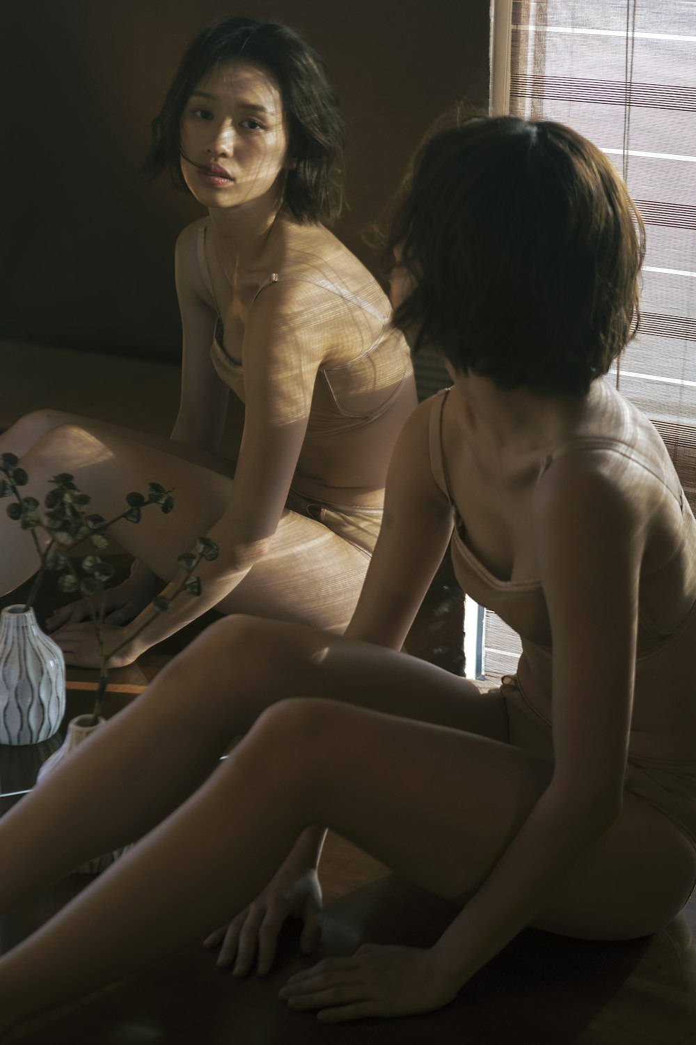 two naked women sitting on a bed in front of a window