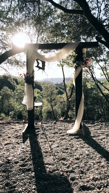 A softly lit outdoor wedding arch adorned with white flowers and greenery, set against a sunset sky.