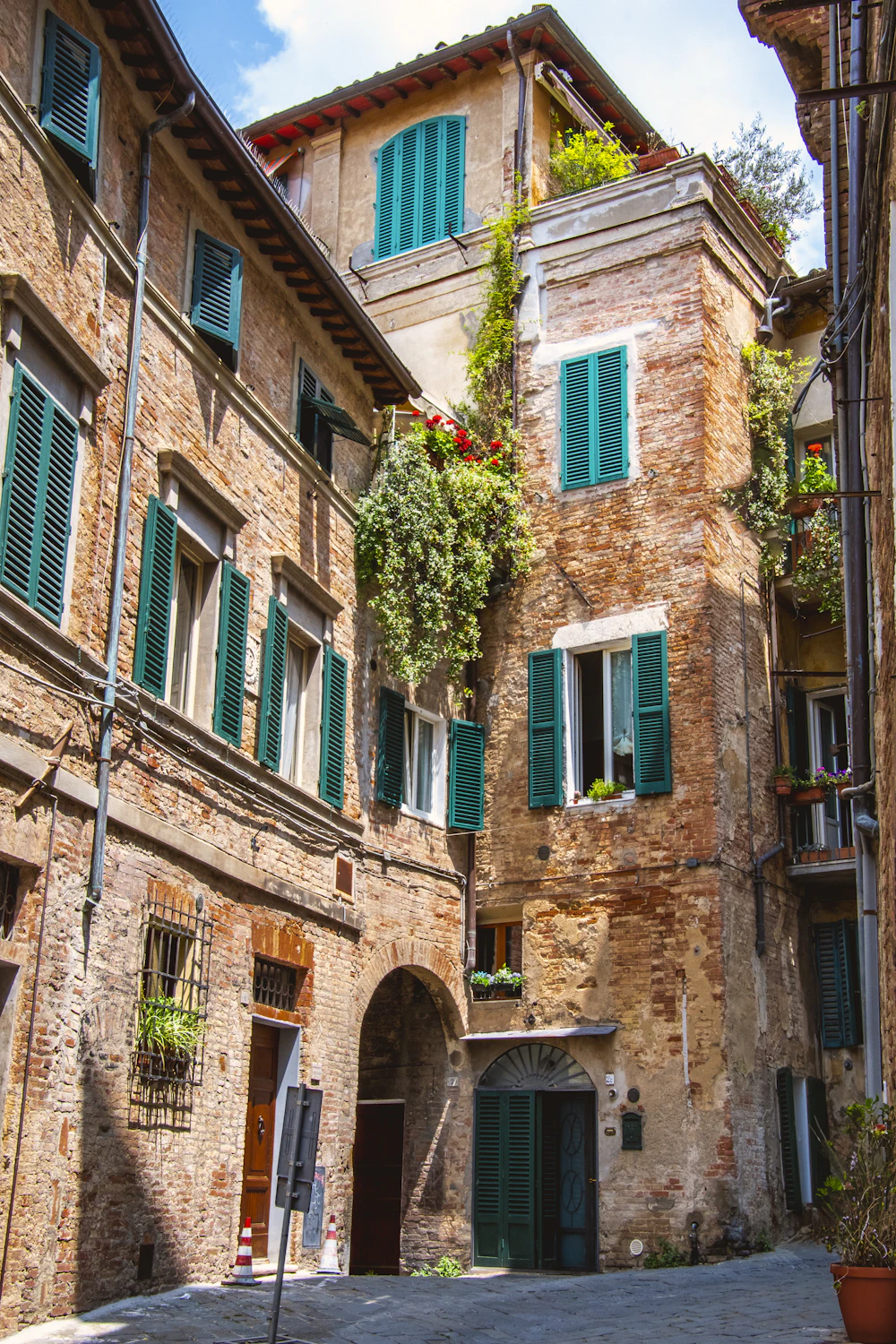 Smalle straat met bakstenen gevels en groene luiken in Siena