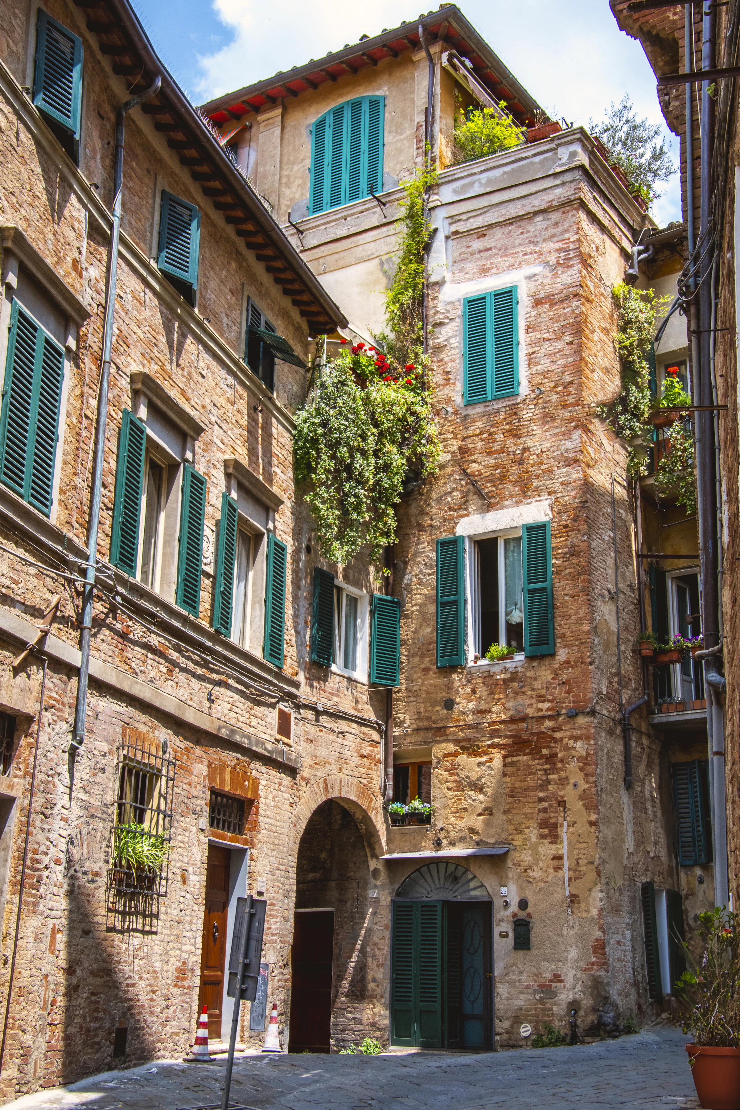 Smalle straat met bakstenen gevels en groene luiken in Siena
