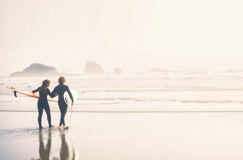 Un couple de personnes tenant des planches de surf sur une plage