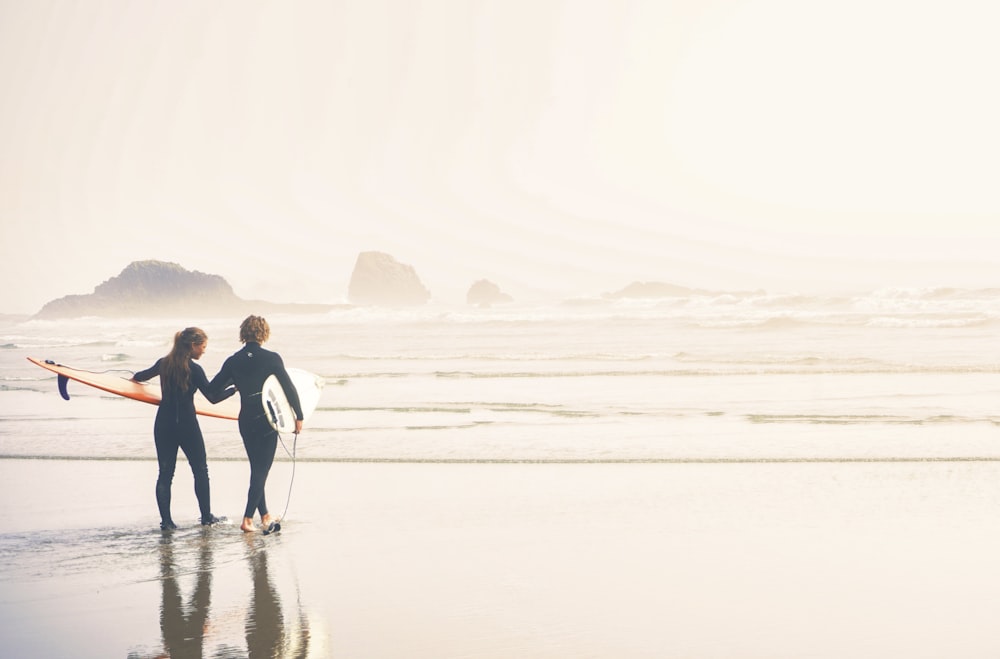 a couple of people holding surfboards on a beach