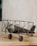 A vintage-style model biplane made of metal is resting on a wooden surface. The design features an old-fashioned propeller and spoked wheels, with an intricate frame structure. The background is a plain, textured wall.