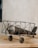 A vintage-style model biplane made of metal is resting on a wooden surface. The design features an old-fashioned propeller and spoked wheels, with an intricate frame structure. The background is a plain, textured wall.