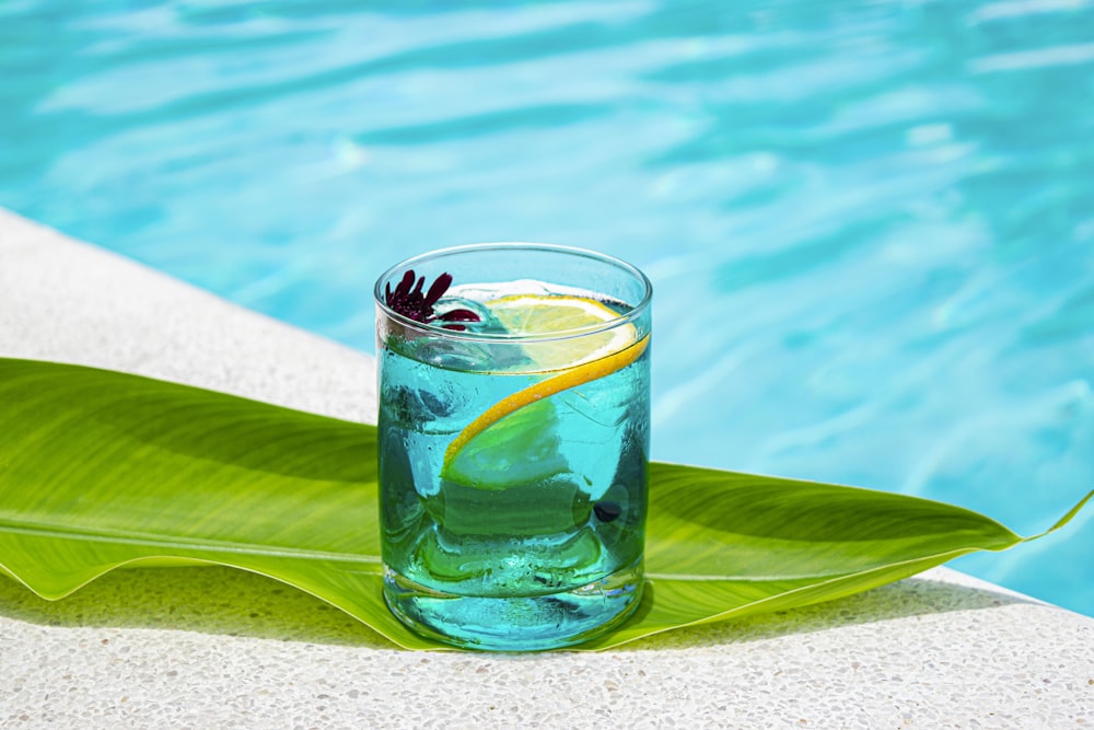 a glass of blue liquid next to a pool