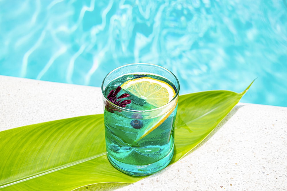 a glass of water with a slice of lemon on a green leaf next to a