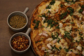 Close-up of a gourmet Indian fusion pizza topped with vibrant spices and fresh herbs on a rustic wooden board.