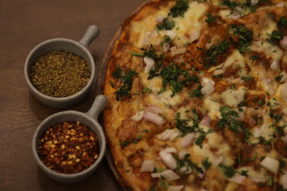 Close-up of a gourmet Indian fusion pizza topped with vibrant spices and fresh herbs on a rustic wooden board.