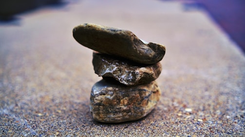 A stack of three distinct rocks balancing on top of each other with a blurred background, giving focus to the intricate textures and shapes of each rock.