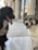Two dogs are sitting on a smooth pavement in an urban setting, one is black with a slightly protruding tongue, and the other has a lighter brown and white coat. Behind them, there is a row of shops with closed shutters and glass doors.