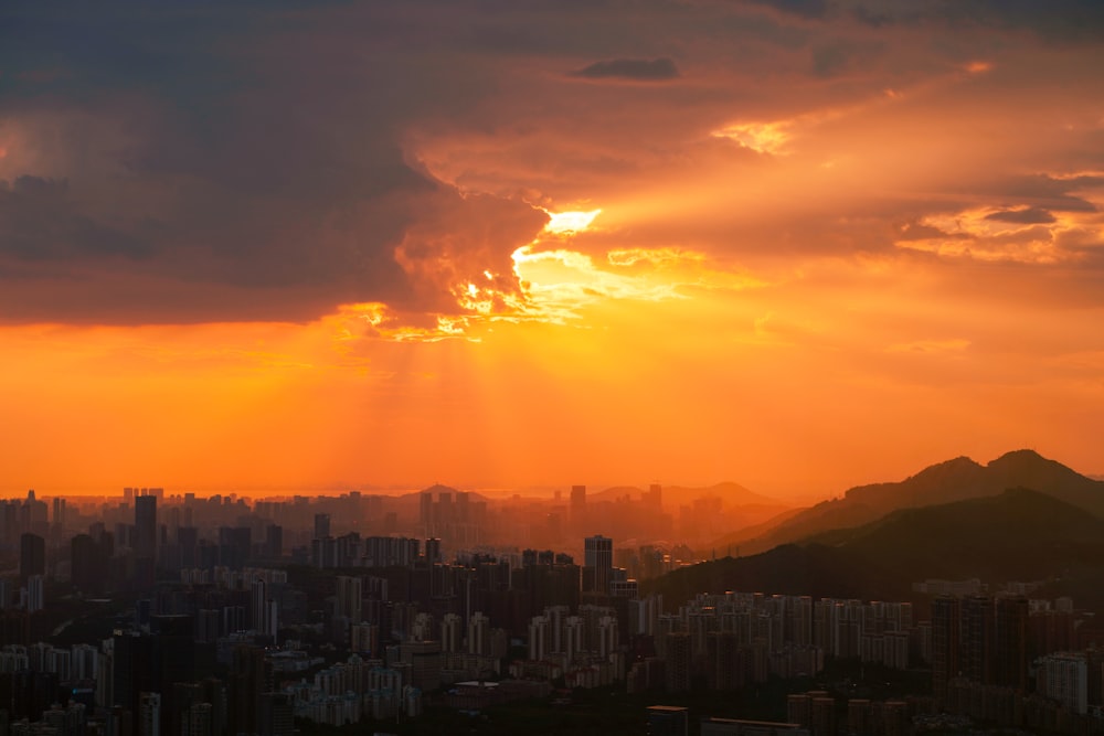 the sun is setting over a city with mountains in the background