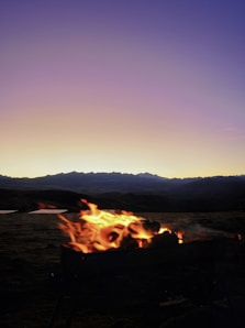 a campfire in the middle of a field with mountains in the background