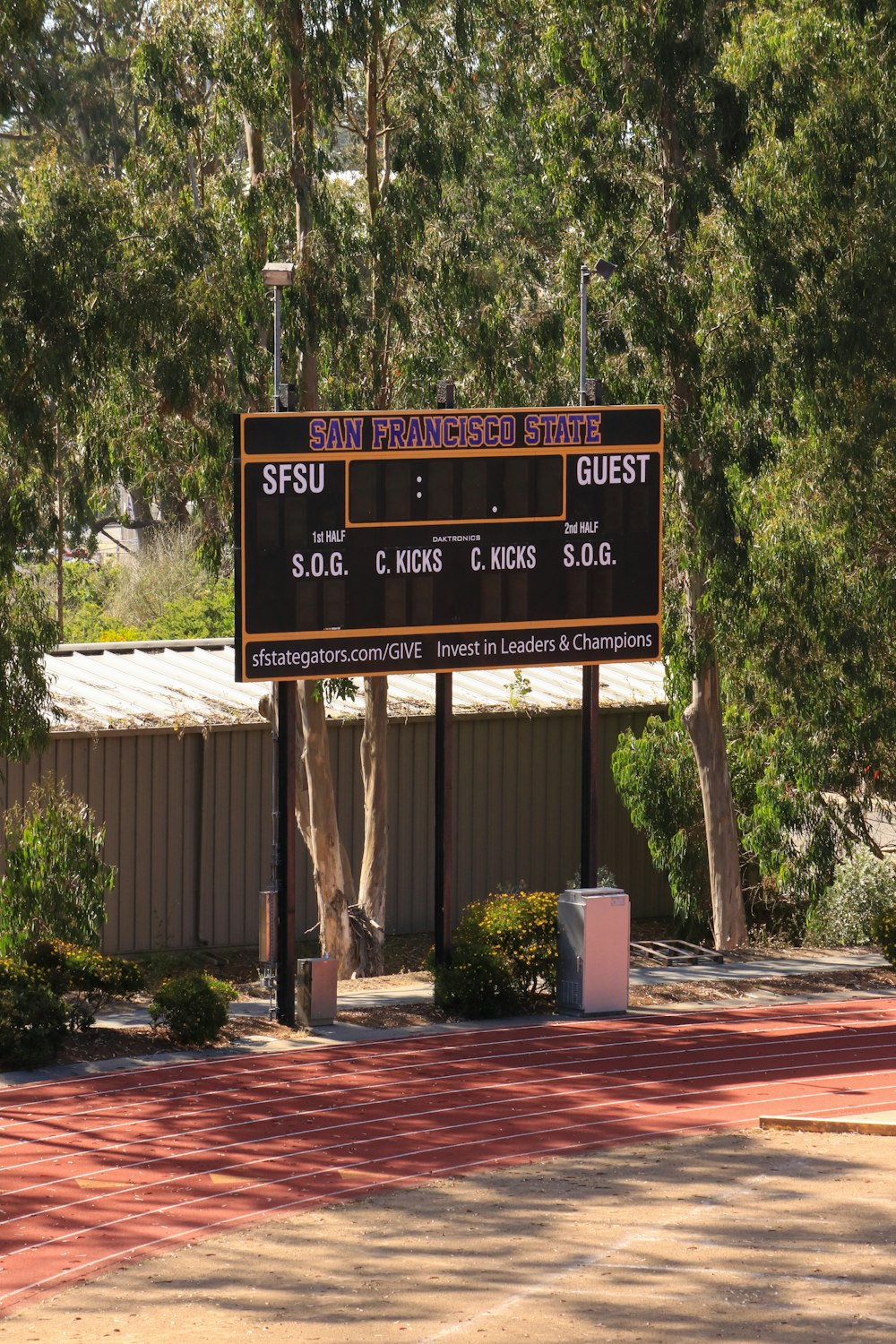 a scoreboard in front of a building with trees in the background