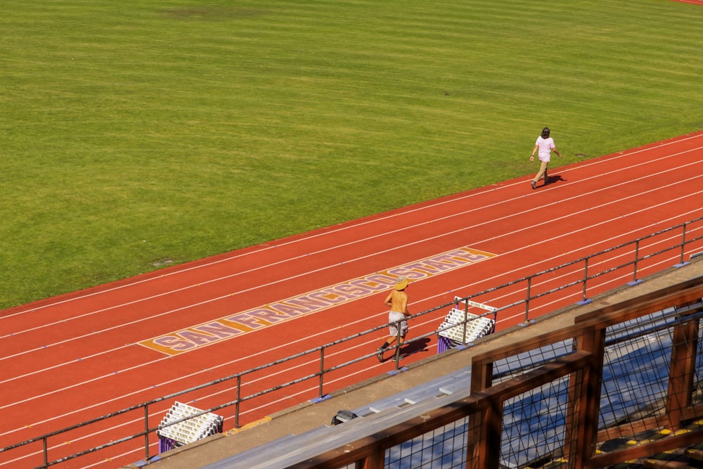 a man walking across a track next to a lush green field