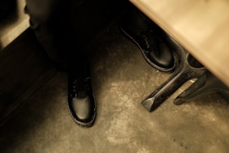 A pair of polished black leather shoes resting on a white floor, catching soft natural light.