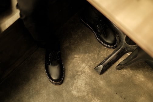 A pair of polished black leather shoes resting on a white floor, catching soft natural light.