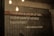 A quote is displayed on a textured concrete wall, illuminated by hanging Edison bulb lights. The text emphasizes the importance of kindness and is attributed to Muhammad SAW.