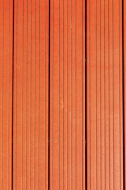 Four vertically aligned wooden planks with a rich brown color. Each plank has evenly spaced grooves running lengthwise, providing a textured appearance. Subtle variations in shade and grain are visible across the surface.
