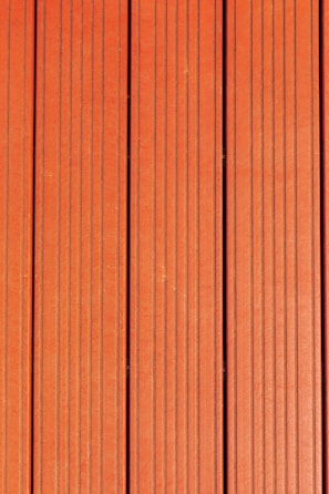 Four vertically aligned wooden planks with a rich brown color. Each plank has evenly spaced grooves running lengthwise, providing a textured appearance. Subtle variations in shade and grain are visible across the surface.