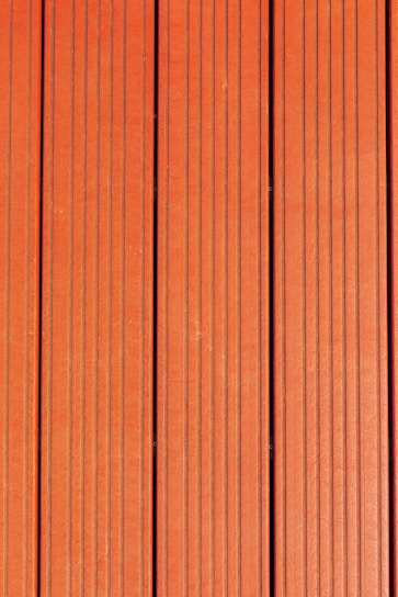 Four vertically aligned wooden planks with a rich brown color. Each plank has evenly spaced grooves running lengthwise, providing a textured appearance. Subtle variations in shade and grain are visible across the surface.