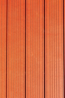 Four vertically aligned wooden planks with a rich brown color. Each plank has evenly spaced grooves running lengthwise, providing a textured appearance. Subtle variations in shade and grain are visible across the surface.