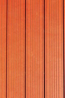 Four vertically aligned wooden planks with a rich brown color. Each plank has evenly spaced grooves running lengthwise, providing a textured appearance. Subtle variations in shade and grain are visible across the surface.
