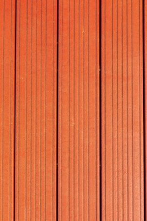 Four vertically aligned wooden planks with a rich brown color. Each plank has evenly spaced grooves running lengthwise, providing a textured appearance. Subtle variations in shade and grain are visible across the surface.