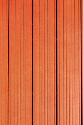 Four vertically aligned wooden planks with a rich brown color. Each plank has evenly spaced grooves running lengthwise, providing a textured appearance. Subtle variations in shade and grain are visible across the surface.