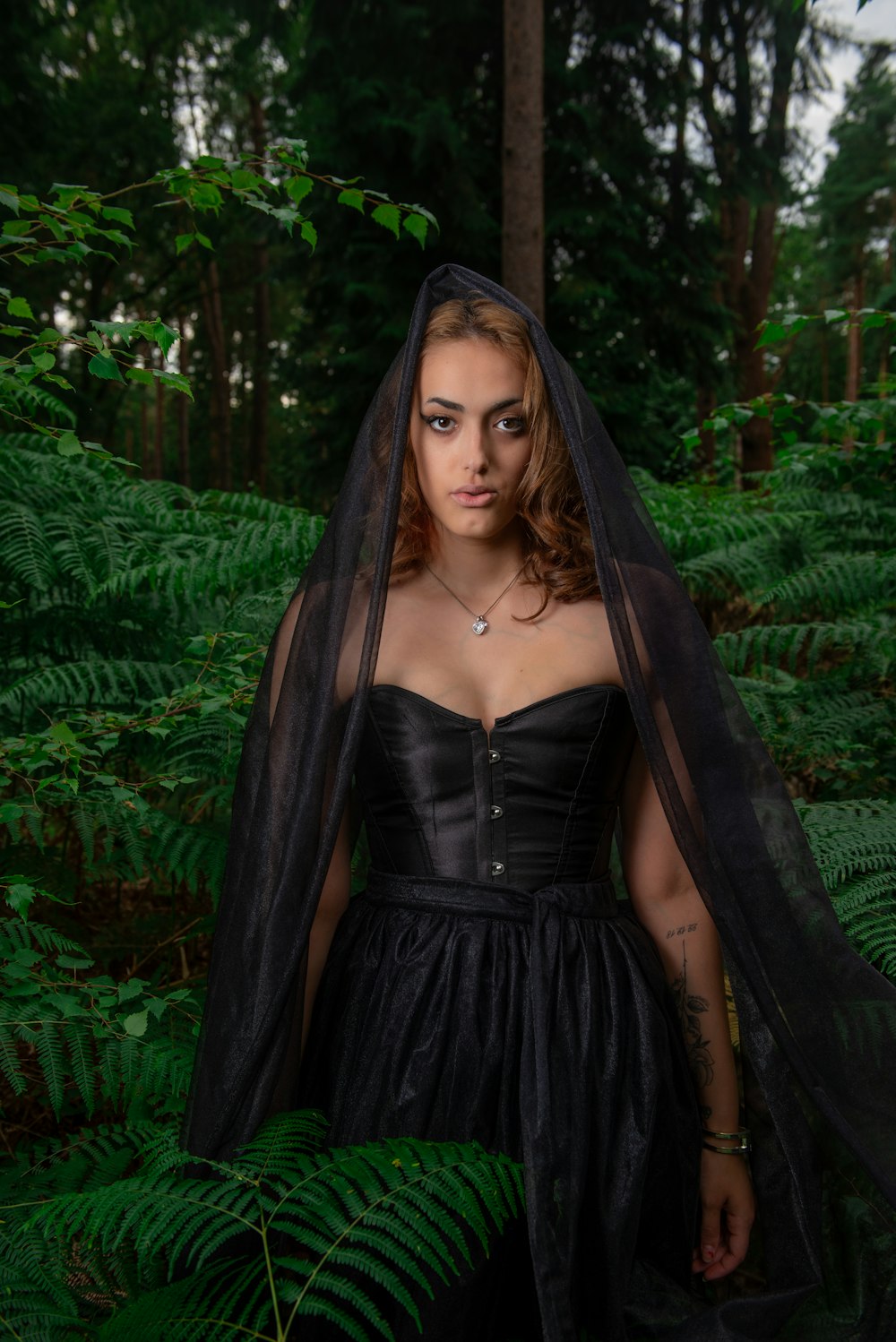 a woman wearing a black corset and veil in a forest