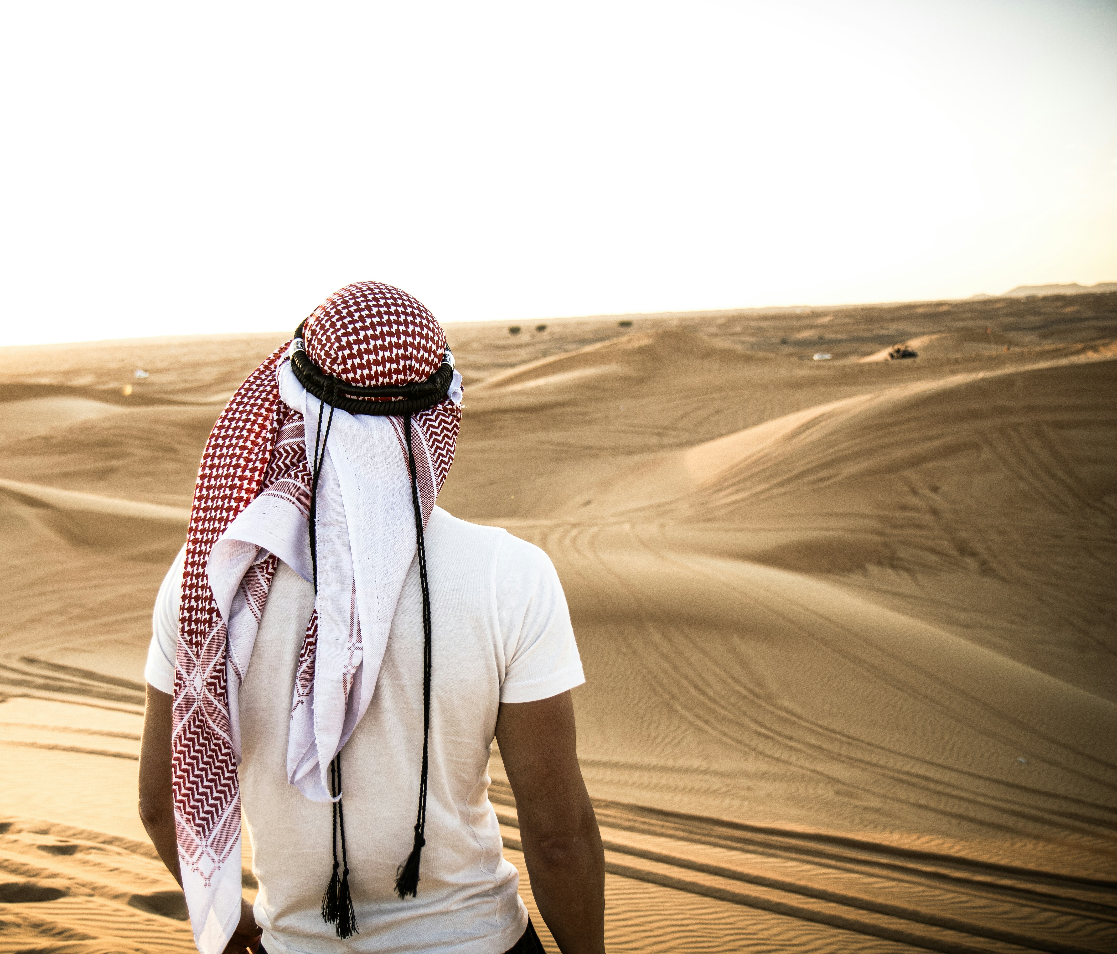 a man in a white shirt and a red and white scarf walking in the desert