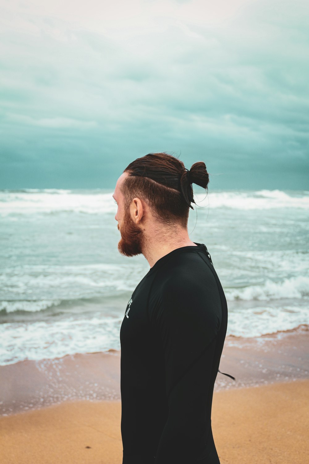 a man with a ponytail standing on the beach