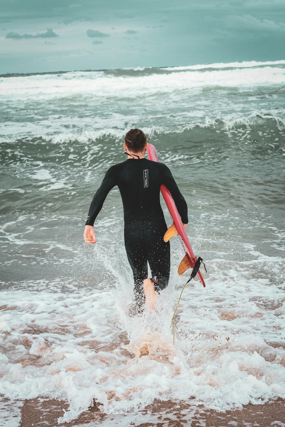 a man in a wet suit carrying a surfboard into the ocean