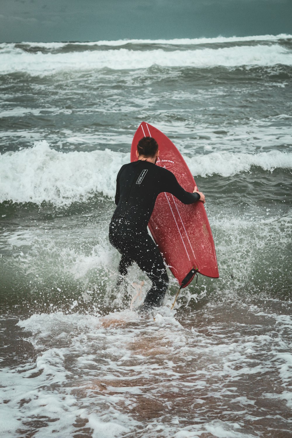 a man in a wet suit carrying a surfboard into the ocean