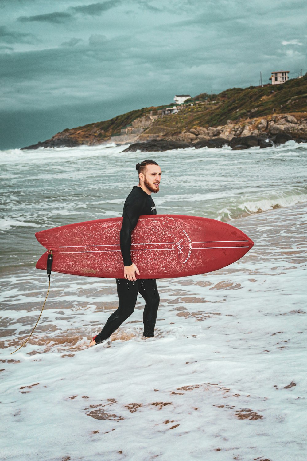 a man in a wet suit carrying a red surfboard