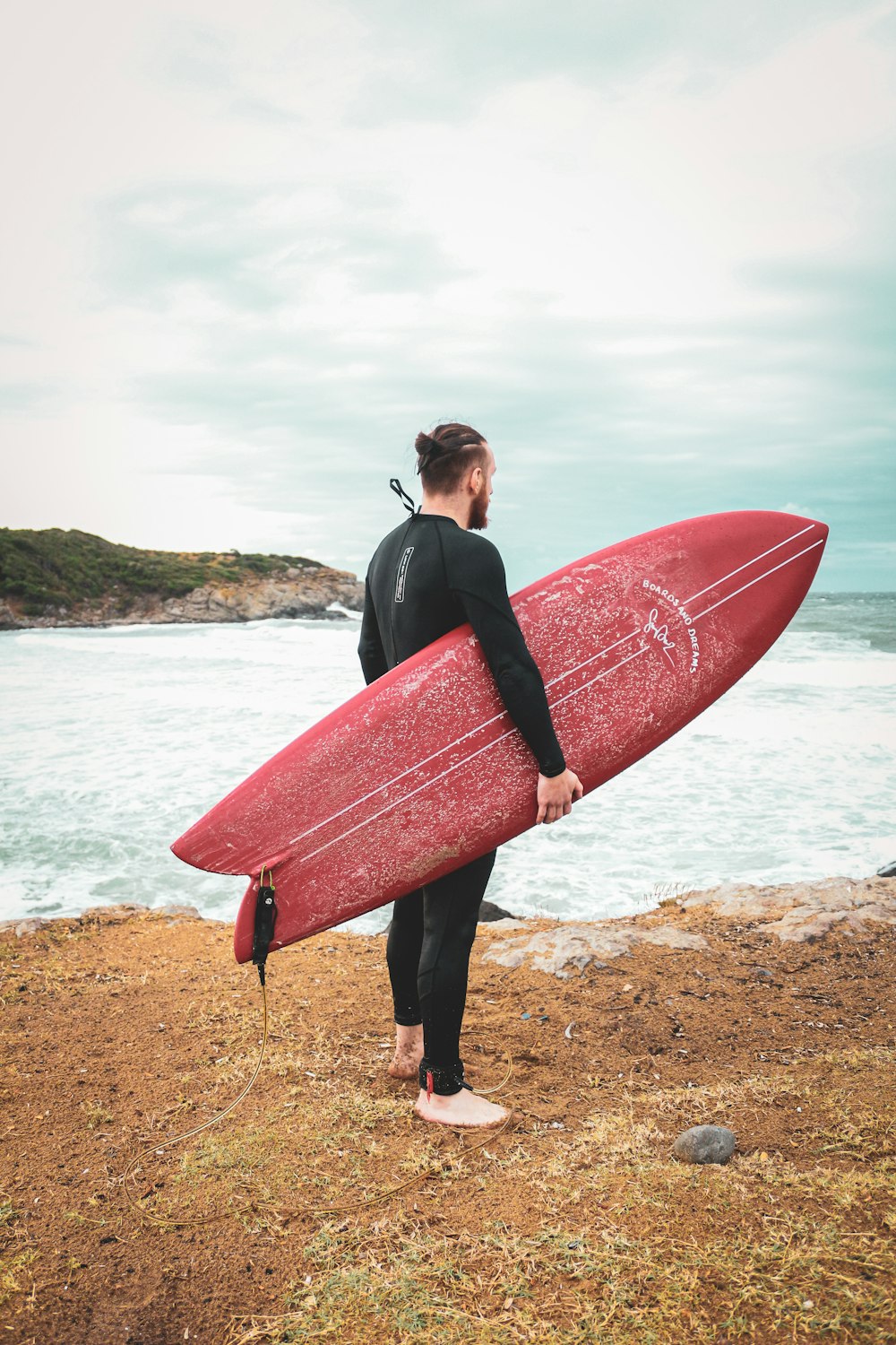 a man holding a red surfboard on top of a sandy beach