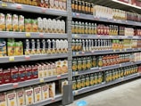 Shelves stocked with various brands and flavors of packaged fruit juices. The cartons are neatly arranged and display a variety of fruit illustrations, indicating different juice flavors. The shelves are labeled with price tags, and the atmosphere resembles a well-organized grocery store aisle.