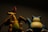 Two collectible figurines are positioned side by side in a dimly lit environment, casting subtle shadows. The first is a dragon with an orange body, wings extended, and a greenish belly. The second figure resembles a large, blue and cream-colored creature with a sleepy expression. Both figures are depicted with detailed features.