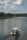 A small motorboat with a canopy is traveling along a calm river surrounded by lush green trees. Fluffy clouds dot the blue sky, creating a serene and peaceful atmosphere.