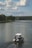 A small motorboat with a canopy is traveling along a calm river surrounded by lush green trees. Fluffy clouds dot the blue sky, creating a serene and peaceful atmosphere.