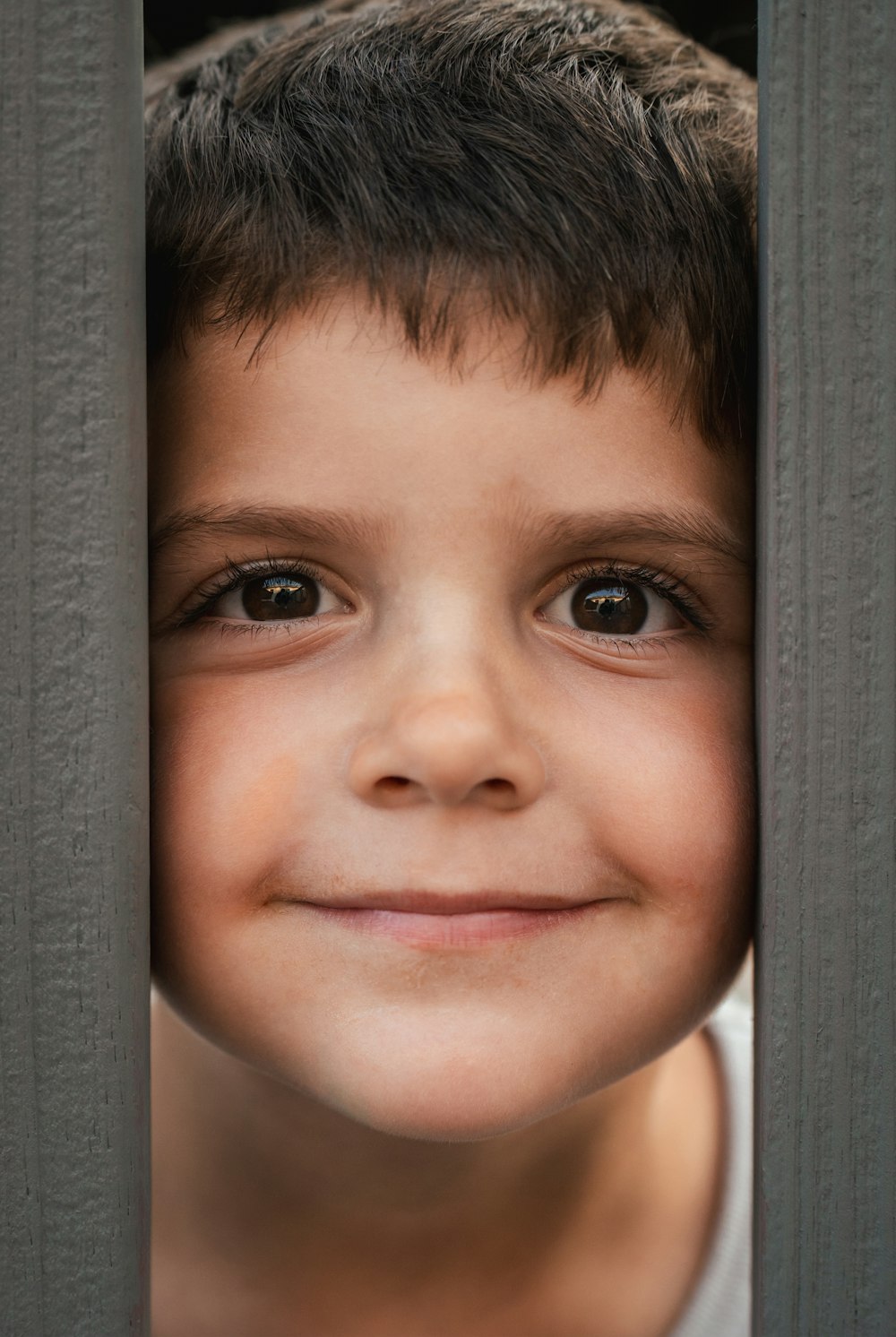 a young boy is smiling through the bars of a fence