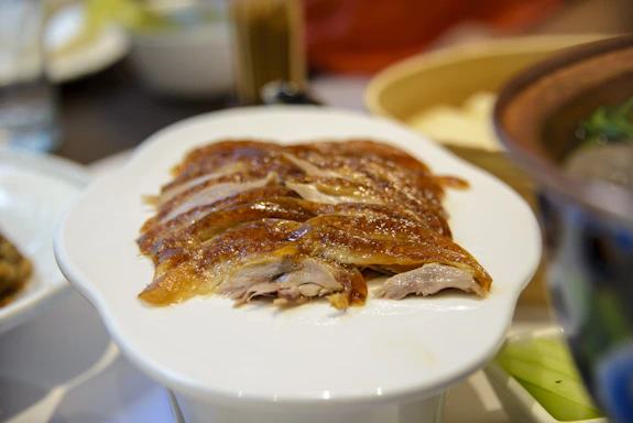 A beautifully plated roast duck with crispy skin, surrounded by colorful seasonal vegetables on a dark green tablecloth.