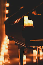A grand piano and candles are lit in a dark room