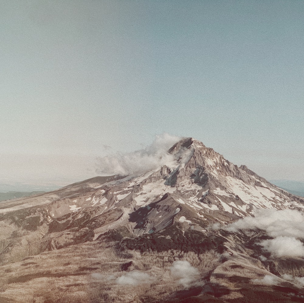 a mountain covered in snow and clouds under a blue sky