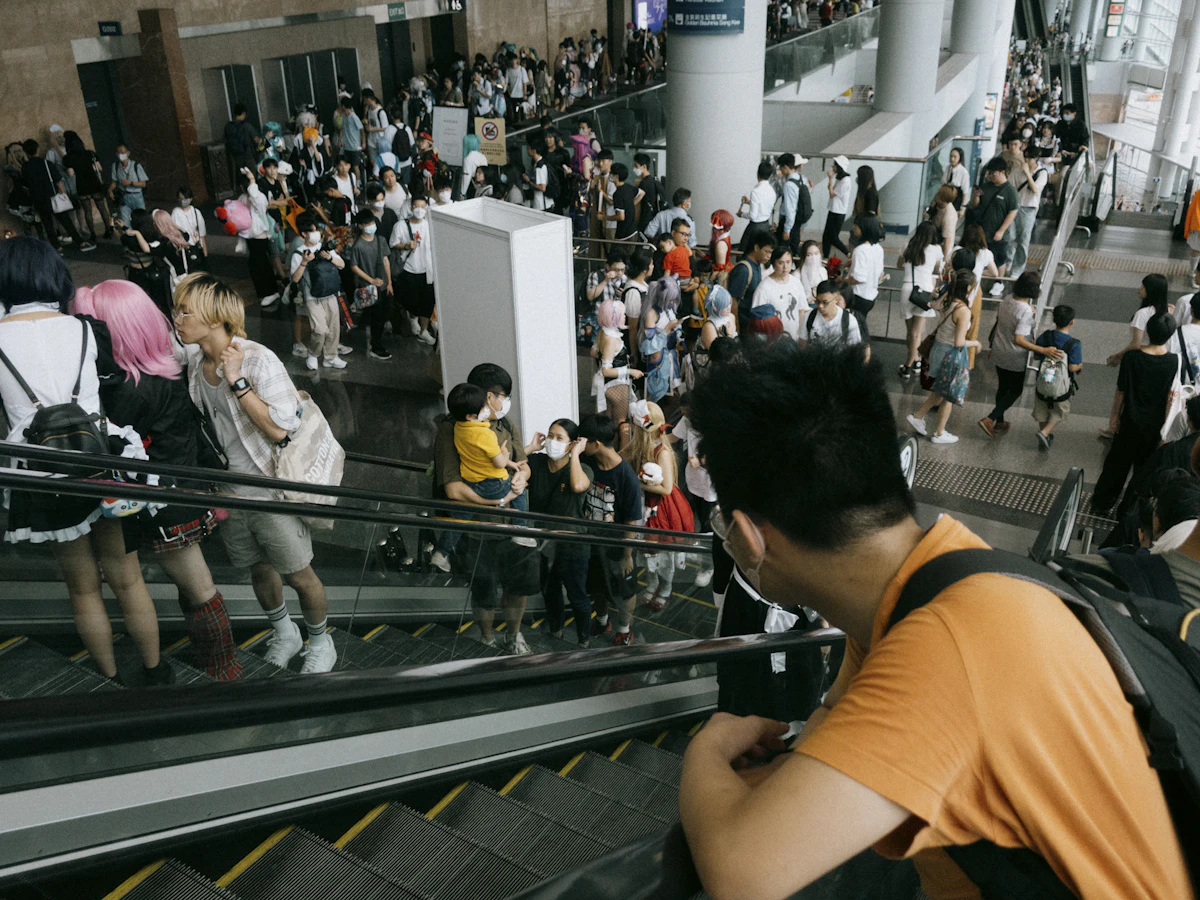 Kerumunan otaku Asia berkumpul di area eskalator anime convention dengan banyak penggemar membawa merchandise berwarna-warni