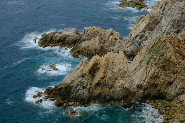 A rocky coast with blue water and green plants — Huatulco, Mexico