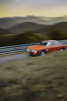 A dynamic shot of a red convertible speeding along a mountain highway at sunset.