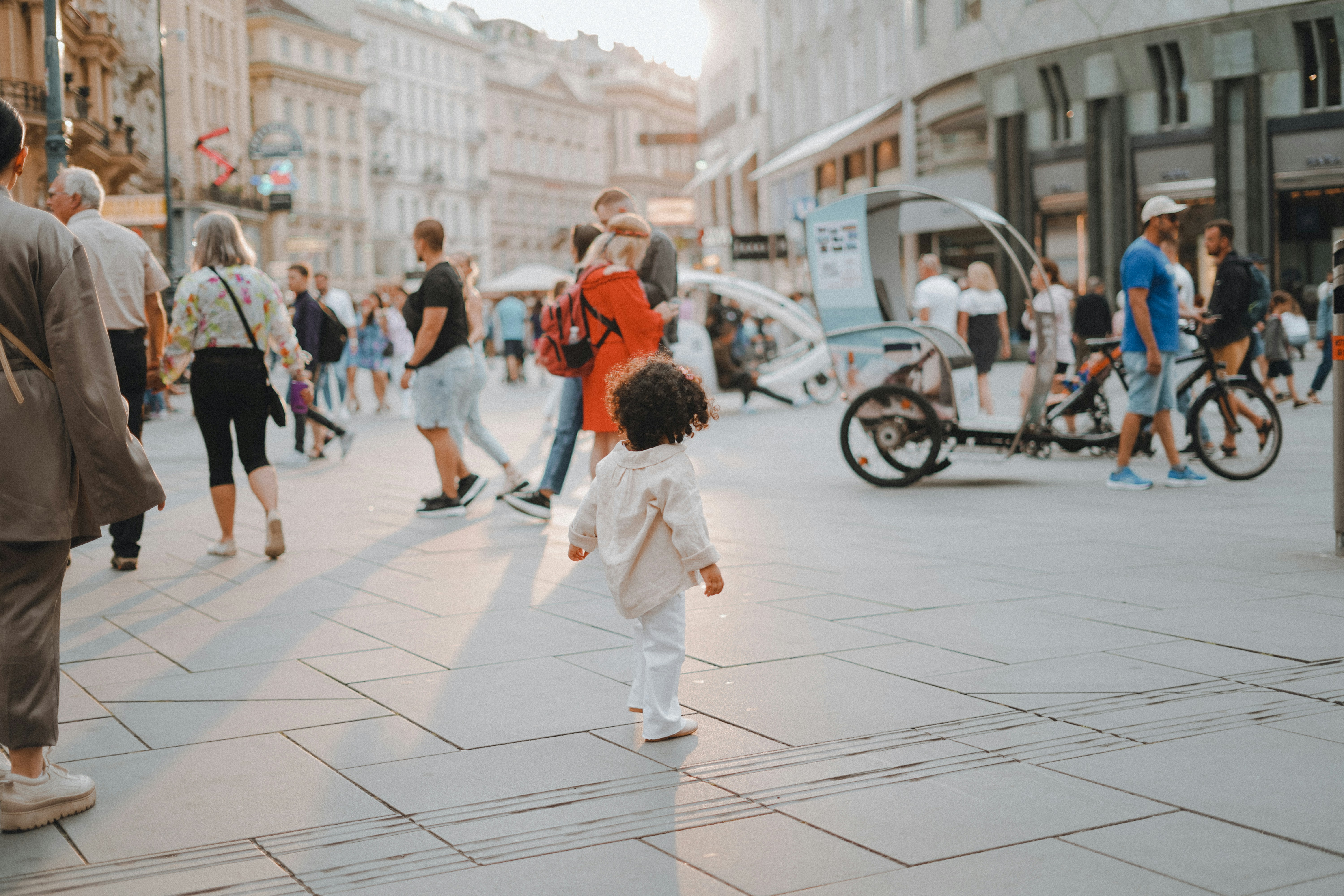 a little girl walking down a street next to a crowd of peopleby Lala Azizli