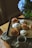 A tray of freshly baked cinnamon rolls, some topped with icing, sits on a wooden table next to a patterned cloth. A cup of coffee is placed in front of the tray, and a vibrant green glass vase holds a bouquet of blue hydrangeas beside it.