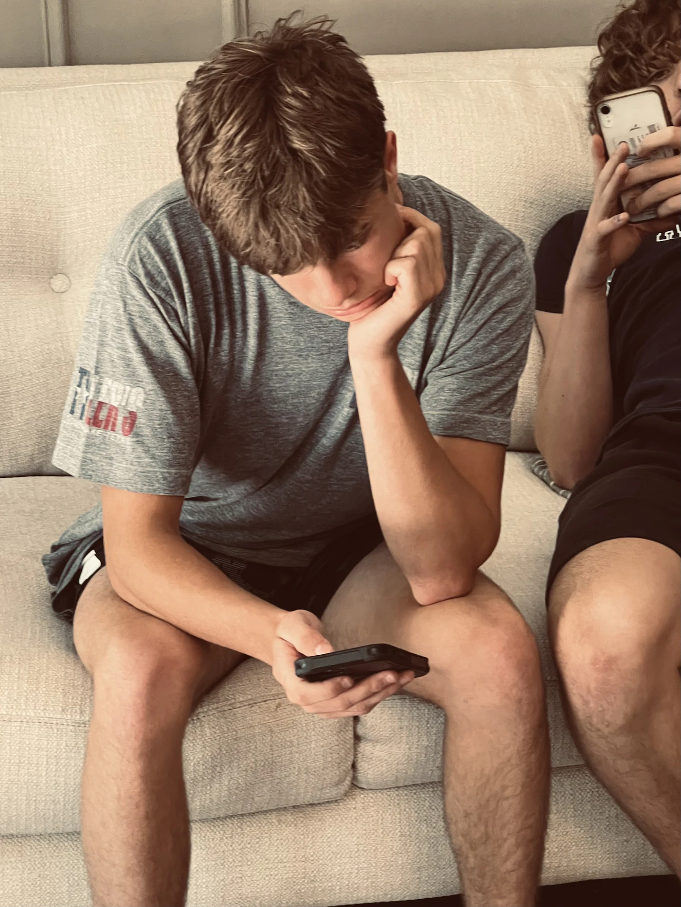 Dos chicos jóvenes sentados en un sofá, uno de ellos mirando su móvil