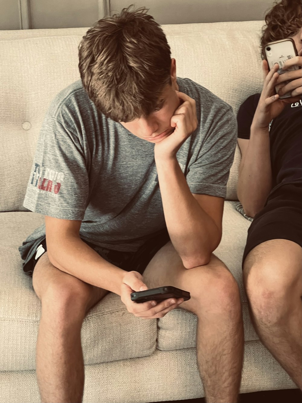 a man sitting on a couch next to another man holding a cell phone